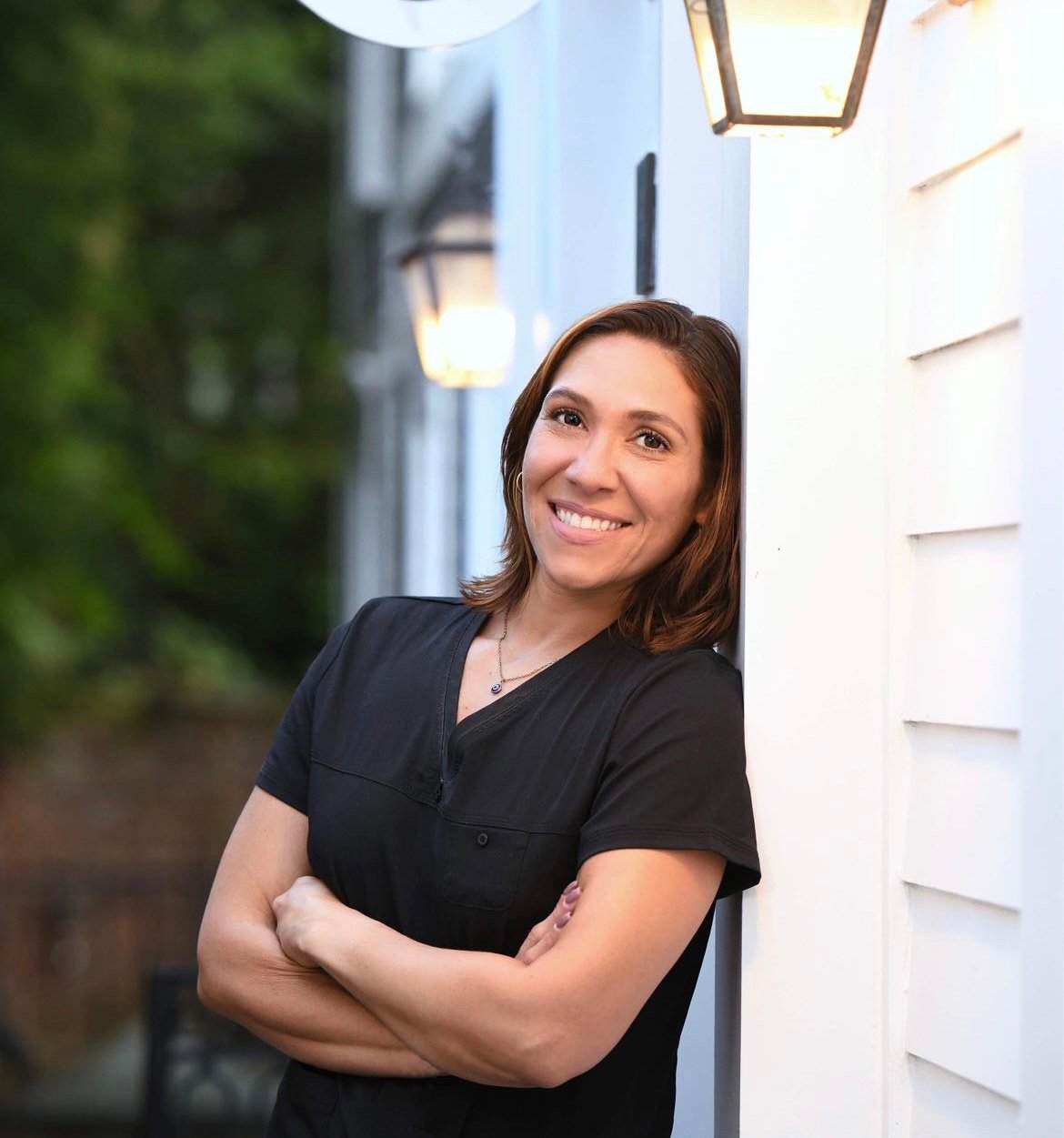 Smiling professional in black shirt leaning against white wall outdoors
